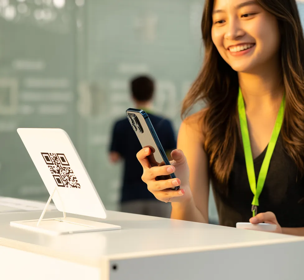 Una ragazza sorridente inquadra con il telefono un QR Code sul banco di accoglienza di un evento
